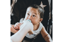 An Asian baby being bottle fed in a stroller.